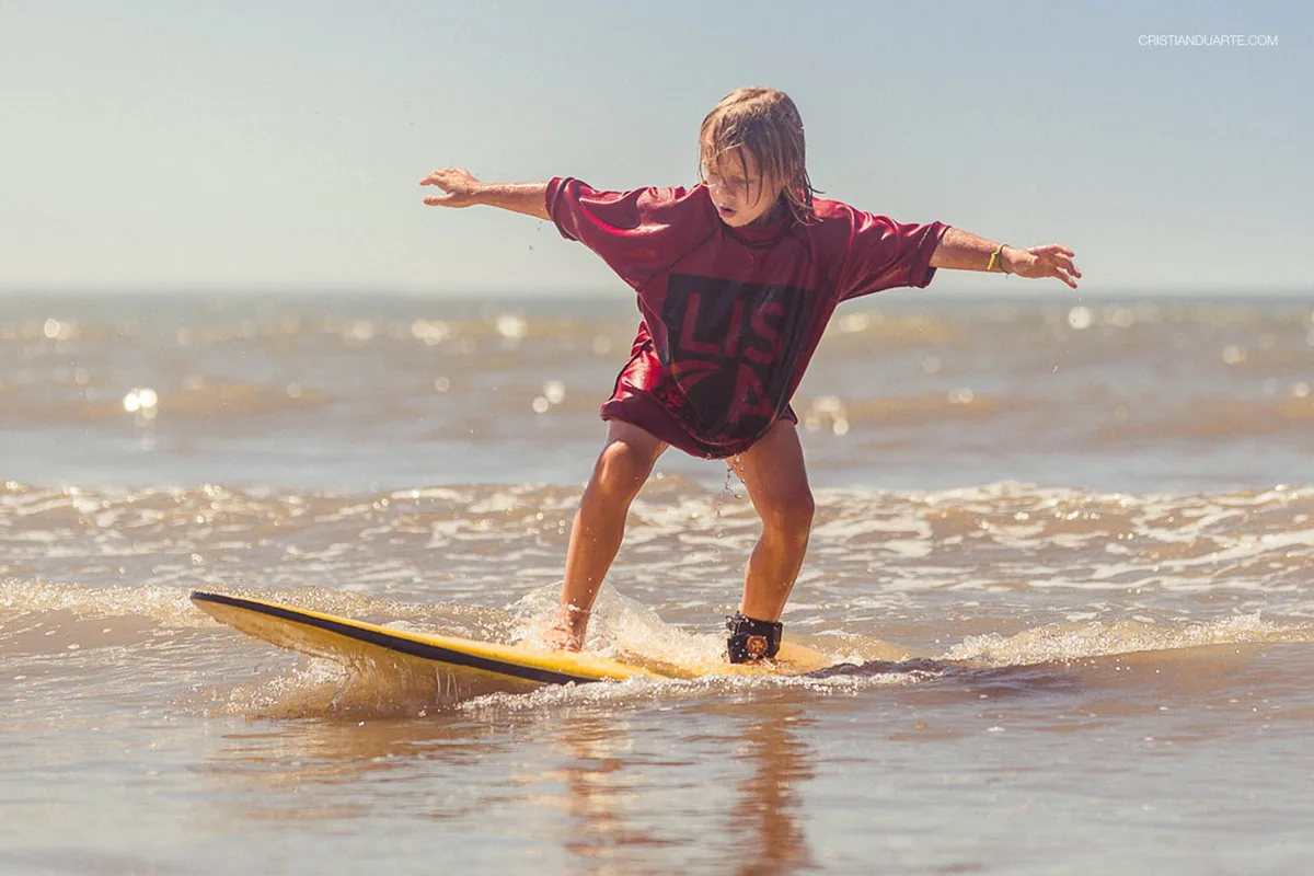 Crianças da Kssino Surf Escola em cima da prancha, na beira do Cassino