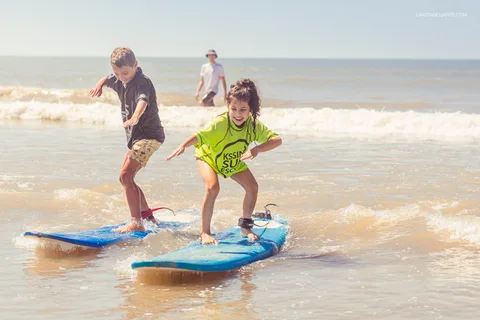 Aluno de surf de pé na prancha, de braços abertos