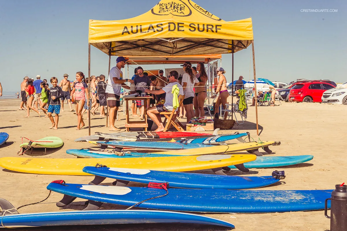 As pranchas da Kssino Surf Escola enfileiradas na areia, na frente da tenda de aulas